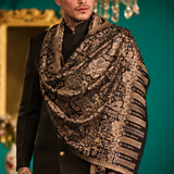 A four-panel collage showing a man modeling a luxurious patterned shawl. The shawl features an intricate floral and paisley design in metallic gold and black, with a matching gold fringe.