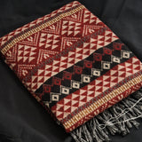 A folded woven throw blanket with a geometric tribal pattern in red, beige, black, and brown, featuring fringed edges, displayed on a dark fabric background.