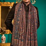 A split-view studio photo shows a person modeling a long patterned shawl or scarf draped over the shoulders. The background is a teal wall with ornate gold-framed mirrors and furniture.