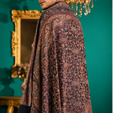 A split-view studio photo shows a person modeling a long patterned shawl or scarf draped over the shoulders. The background is a teal wall with ornate gold-framed mirrors and furniture.