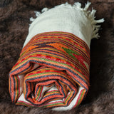 A rolled white woven textile with a colorful striped and geometric patterned band, resting on a dark brown fur surface.