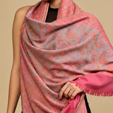 A three-panel model photo showing a woman wearing a large pink shawl with a paisley pattern over a black outfit, against a beige studio background.