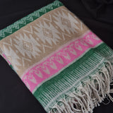 A folded woven throw blanket with a Southwestern geometric pattern in beige, green, pink, and white, featuring fringed edges, displayed on a dark background.