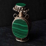 A vintage silver snuff bottle pendant with a green turquoise stone set in the center, placed on a dark textured surface.