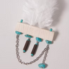 A white feather accessory with an off-white rectangular bar, turquoise-colored beads, silver chains, and dark brown cylindrical beads, photographed on a light gray background.