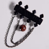 A black gothic-style pendant necklace featuring a bar with faceted spikes, two draped dark metal chains, and a round brown marbled bead pendant, shown on a light gray background.