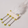 A white feather feather pen with a cream-colored handle, four dangling silver chains, and round lime-green beads, photographed on a light gray background.
