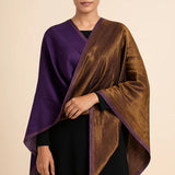A woman modeling a dual-colored wrap shawl with a deep purple border and a metallic bronze-brown main body, styled over a black dress against a solid beige background.