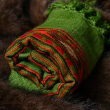 A rolled green woven scarf with red and orange striped accents and fringed edges, displayed on a dark brown fur surface.