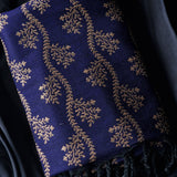 A close-up of a navy blue fabric item, likely a shawl or scarf, featuring an intricate gold floral and vine pattern woven across the surface.