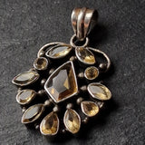 A vintage-style silver pendant featuring a central faceted brown gemstone surrounded by smaller marquise and teardrop-cut brown gemstones, set against a dark textured slate background.