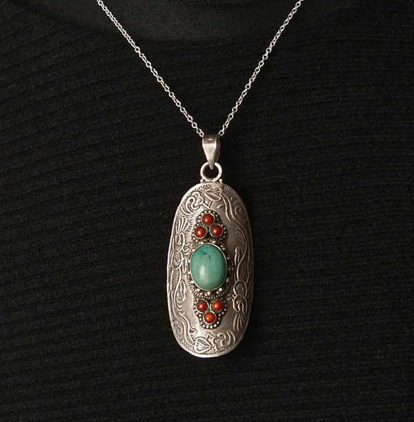 Silver pendant with turquoise and red stones on a black background