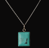 A silver chain necklace with a square pendant featuring a turquoise-colored stone with a black inlay, shown against a solid black background.
