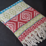 A folded woven throw blanket with a colorful geometric pattern and fringed edges, displayed on a dark background.
