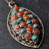 A silver filigree pendant featuring multiple round turquoise and coral stone inlays, photographed close-up against a dark textured background.