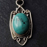 A silver pendant featuring a turquoise stone with intricate vintage designs around it.
