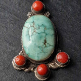A sterling silver pendant featuring a central turquoise stone with coral accents on the sides, set on a dark background.