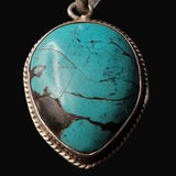 A teardrop-shaped turquoise pendant with a silver-toned braided bezel setting, shown against a solid black background.
